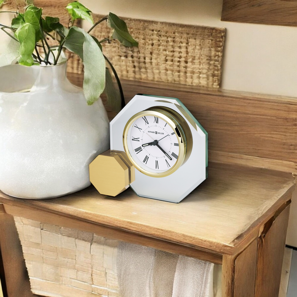 A stylish octagonal clock with a gold accent sits on a wooden table next to a decorative vase and woven basket.