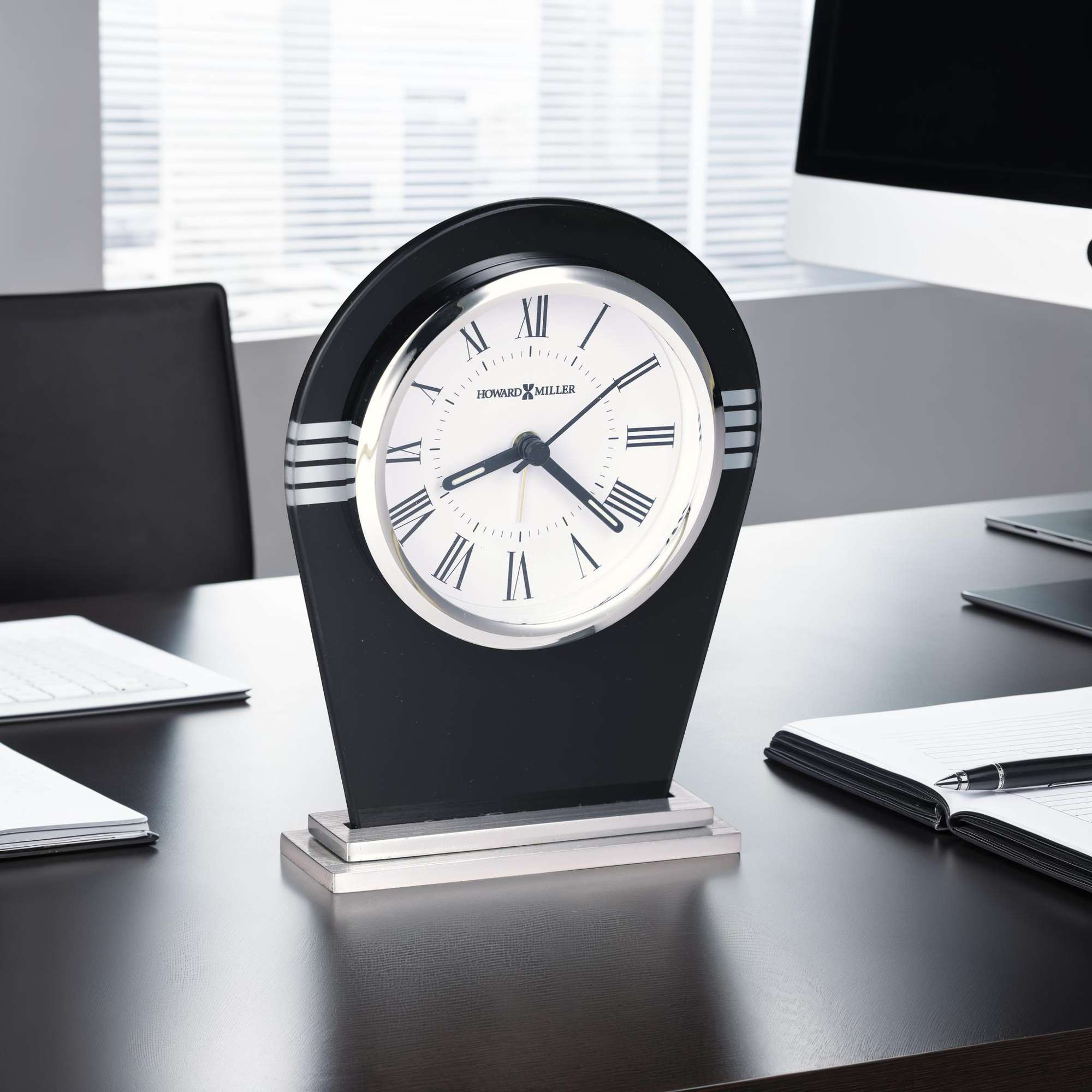A stylish black desk clock with Roman numerals on a modern office desk.