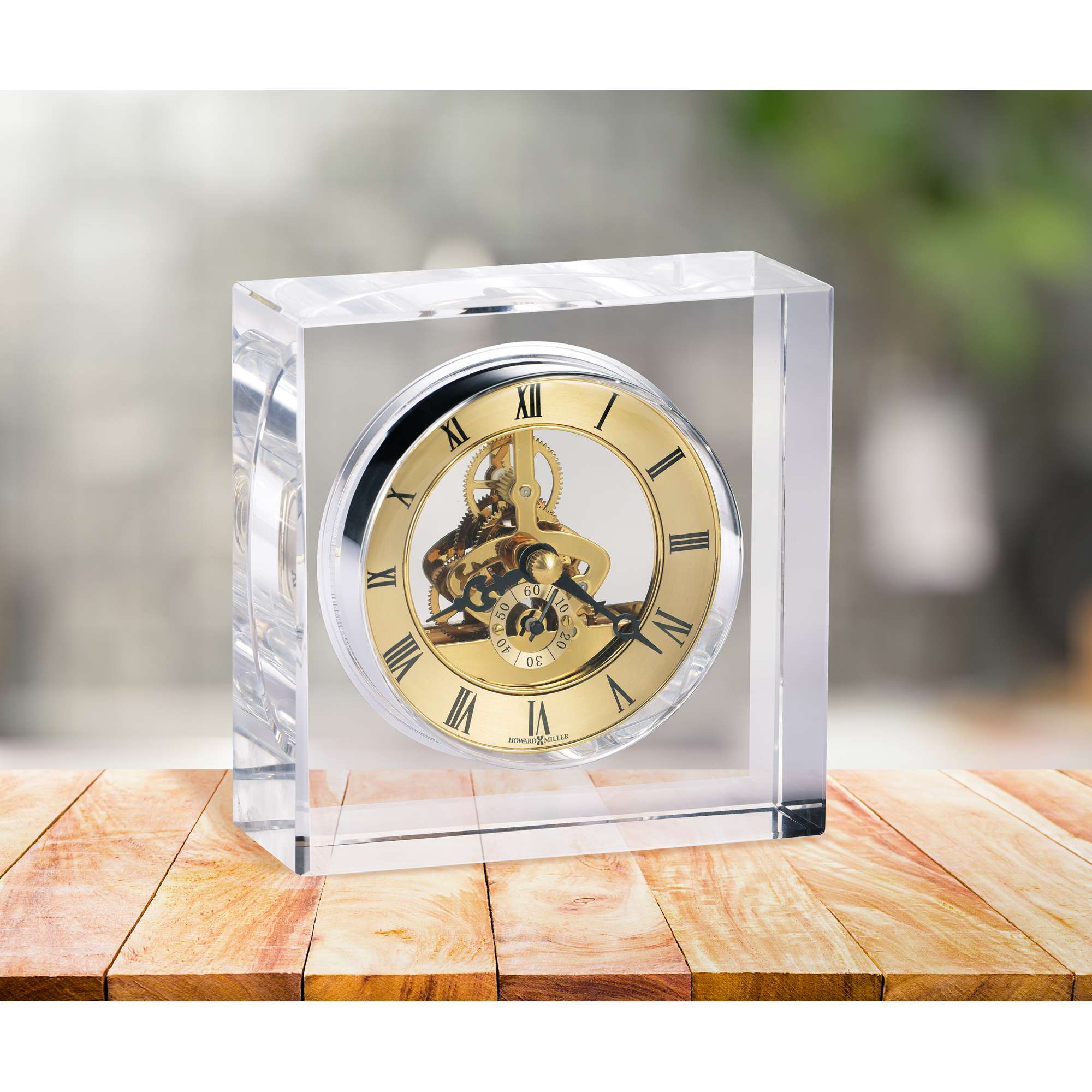 A clear crystal clock with a gold face, set on a wooden table.