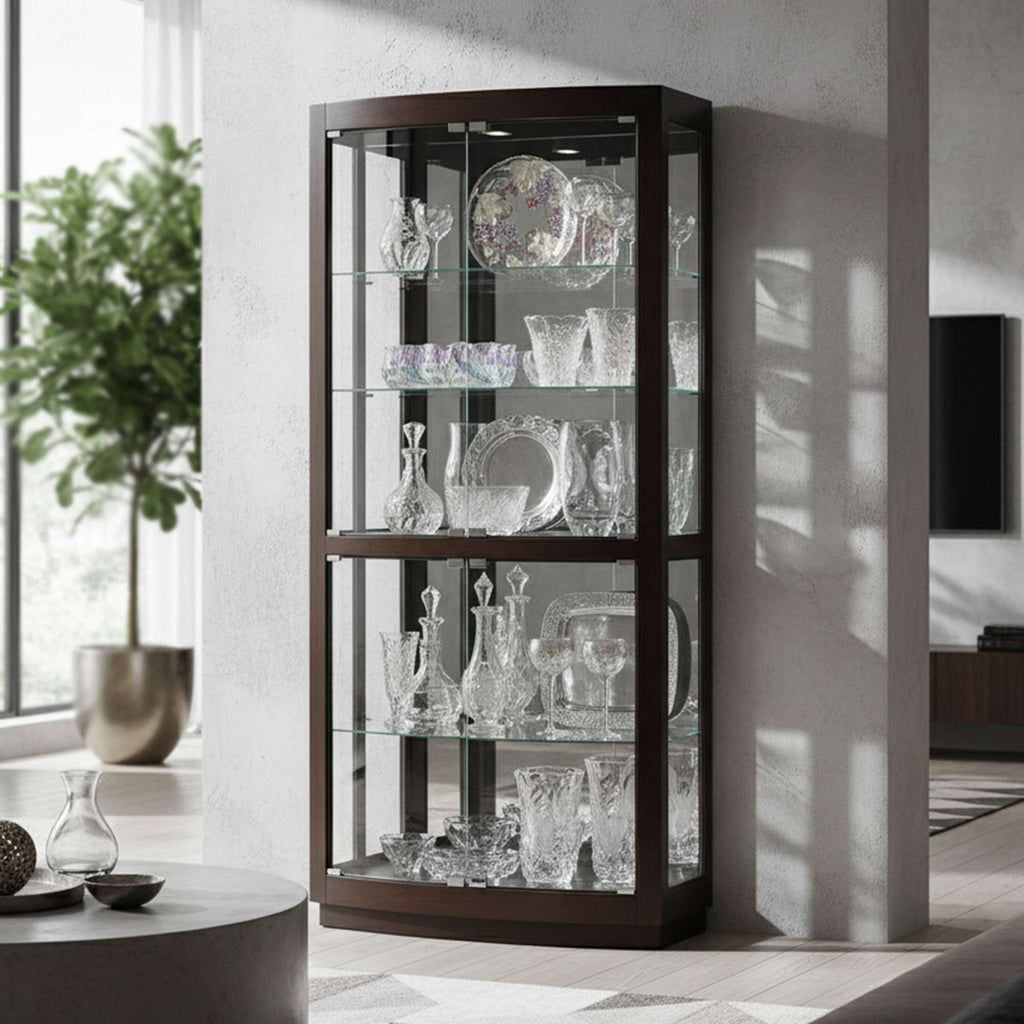 A modern glass display cabinet showcasing various crystal glassware, positioned in a stylish living room with a large plant in the background.