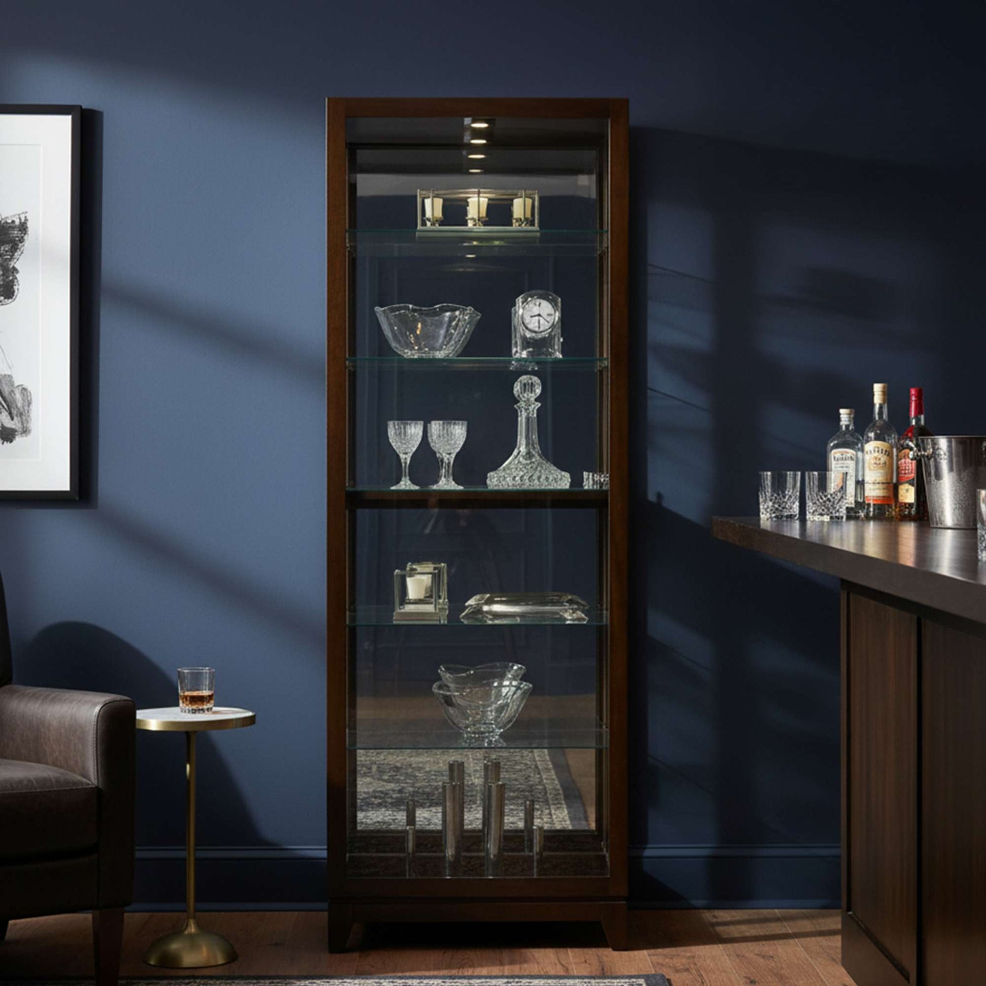 A stylish display cabinet with glass shelves showcasing crystal glassware and decorative items, set against a dark blue wall.