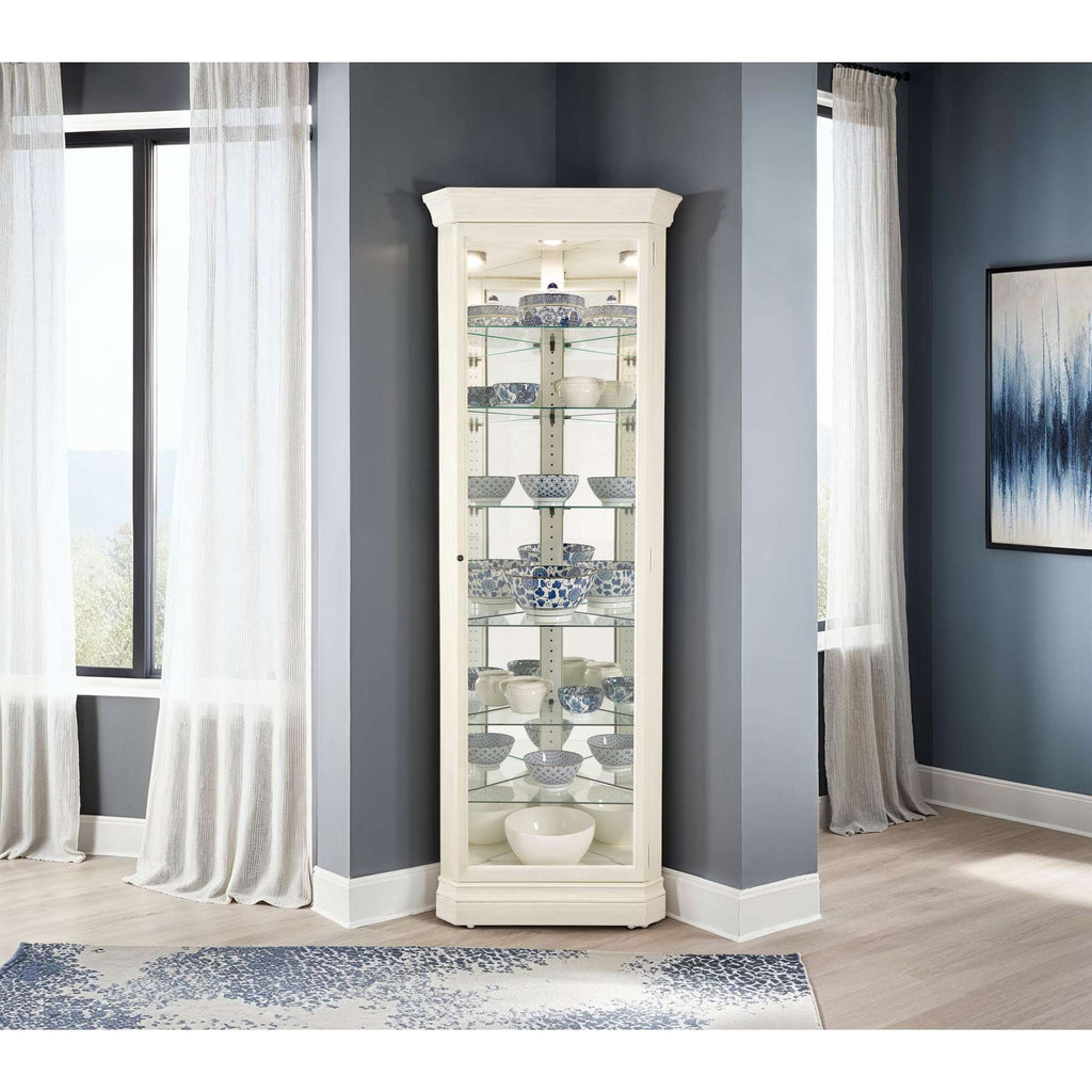 A tall, elegant display cabinet with glass shelves showcasing decorative items, set against a modern, well-lit interior with large windows.