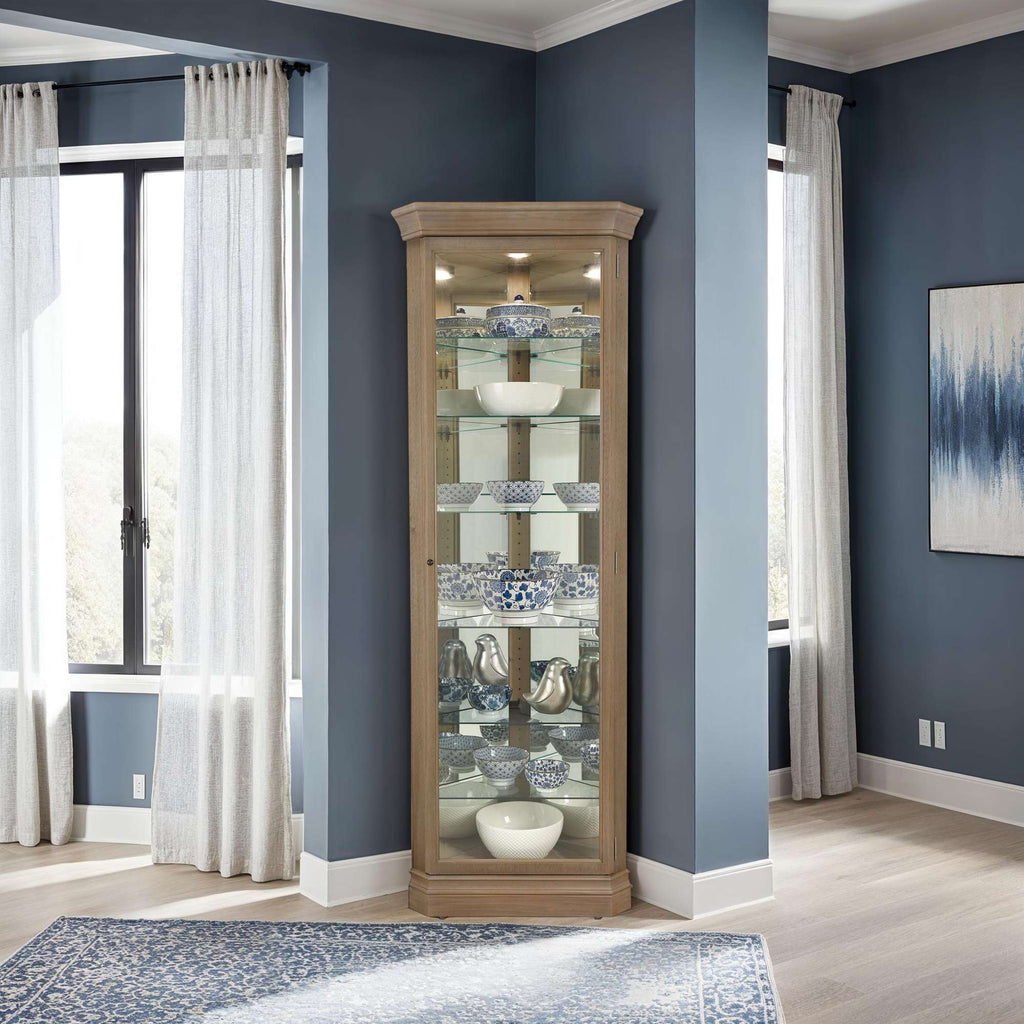 A stylish corner display cabinet in a modern living room with large windows and blue walls.
