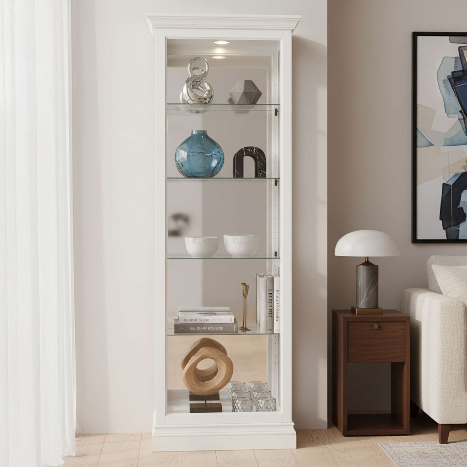 A tall, white display cabinet featuring glass shelves filled with decorative items, positioned next to a side table and framed artwork.