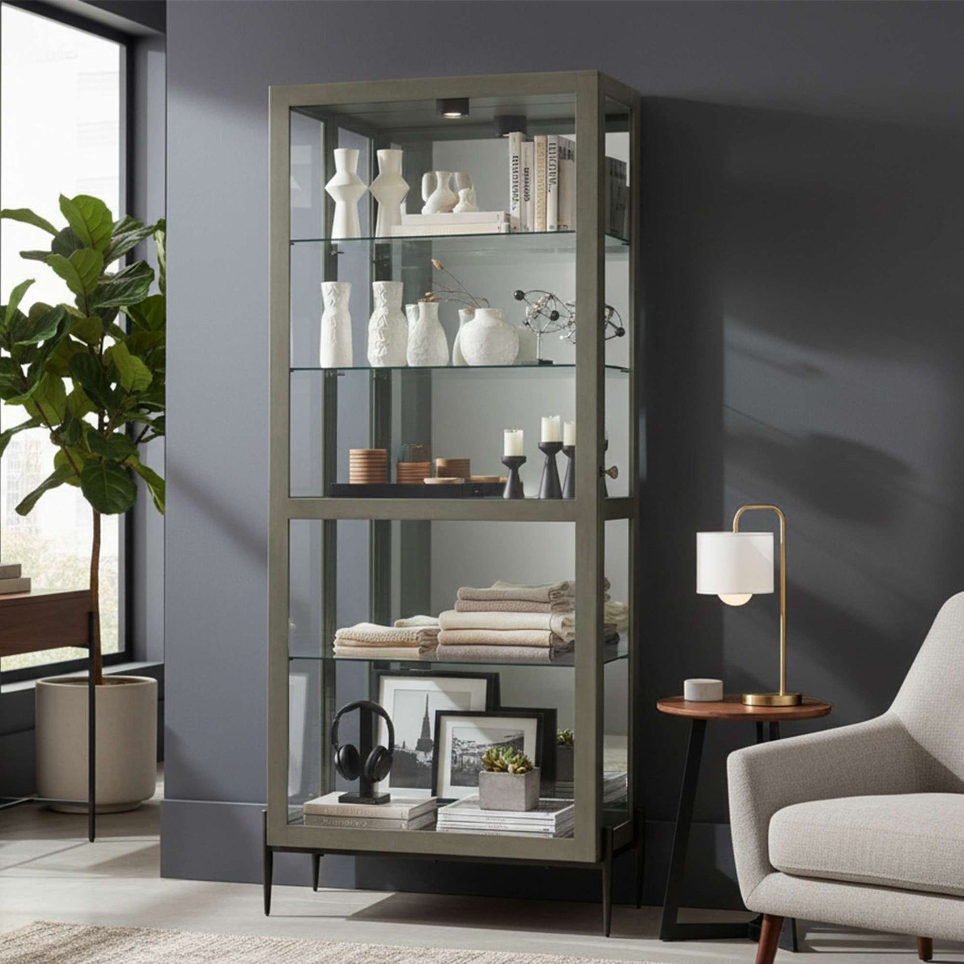 A modern glass display cabinet showcasing various decorative items and books in a stylish interior setting.