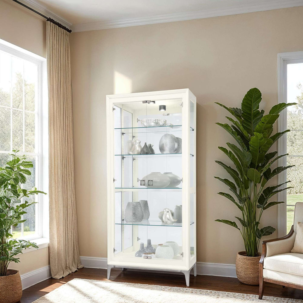 A display cabinet with glass shelves showcasing decorative items, next to a large potted plant in a bright, sunny room.