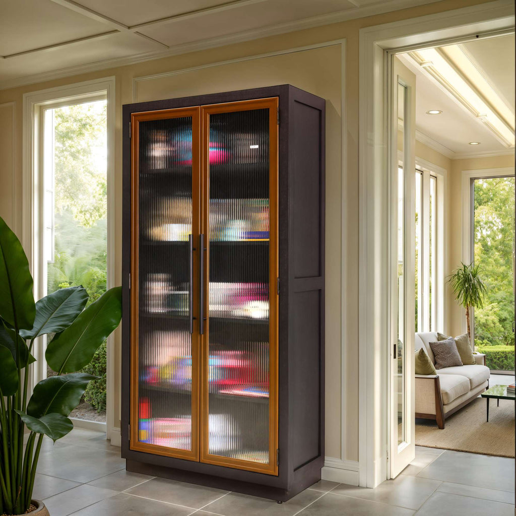 A modern glass-front cabinet displaying colorful items, situated in a bright room with large windows and a view of greenery.