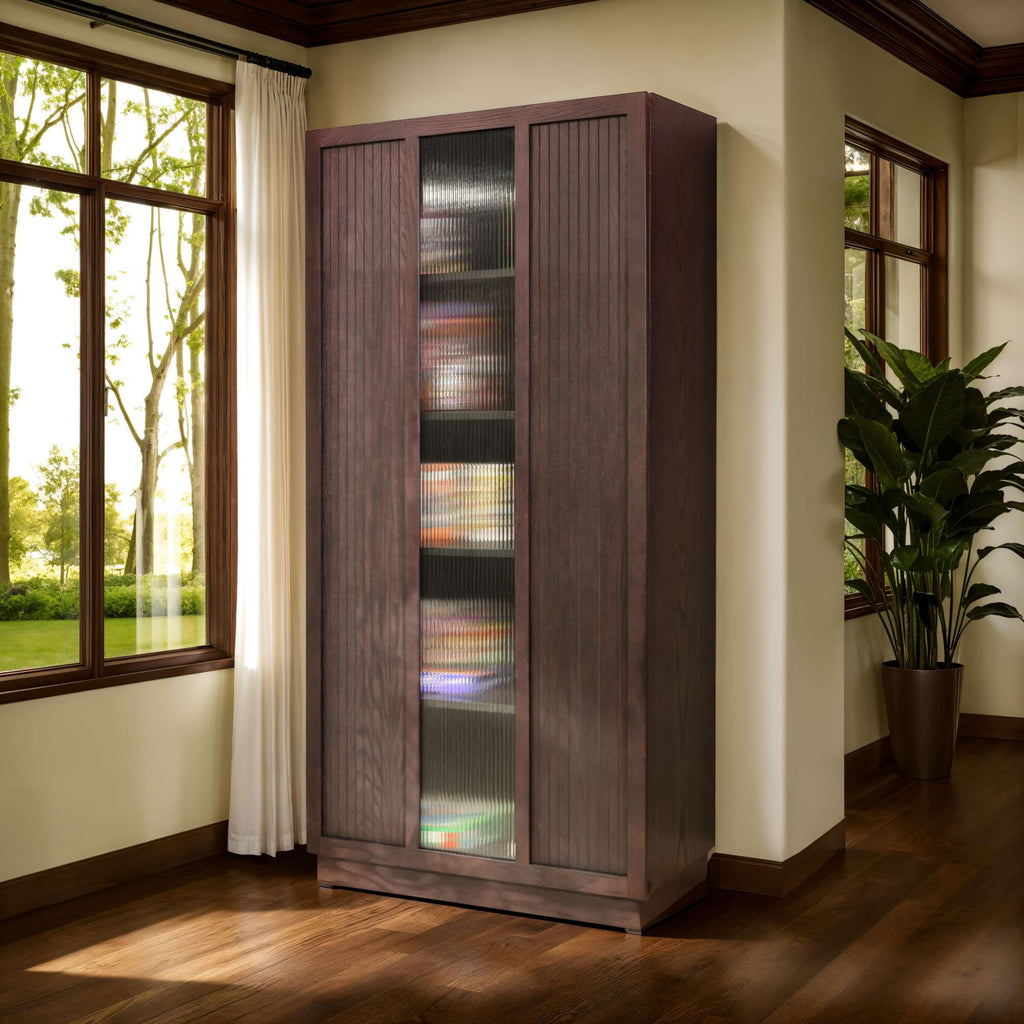A tall wooden cabinet with glass doors, situated in a well-lit room next to large windows and a potted plant.