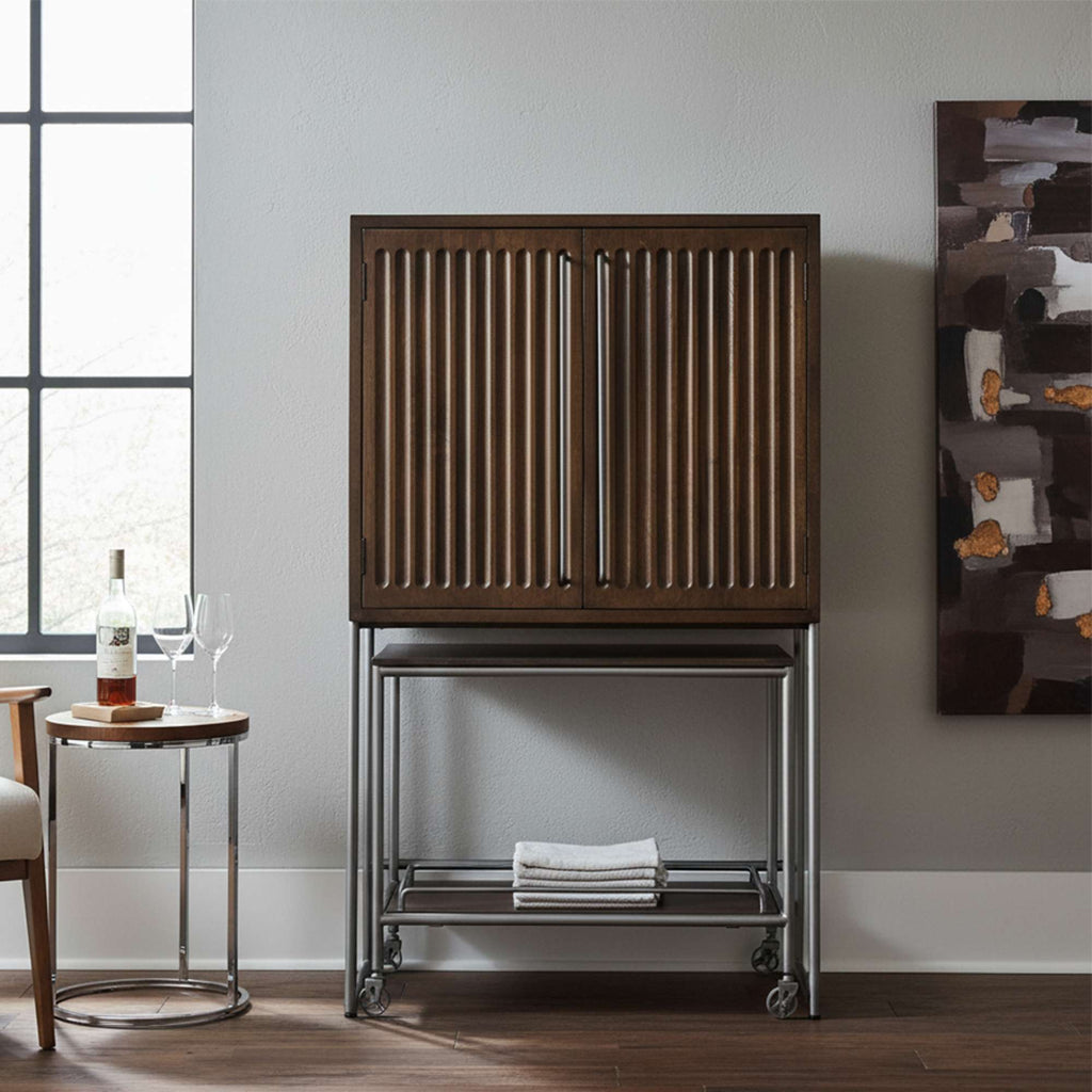 Wooden cabinet with ribbed doors on a metal frame, next to a small round table and a modern artwork.