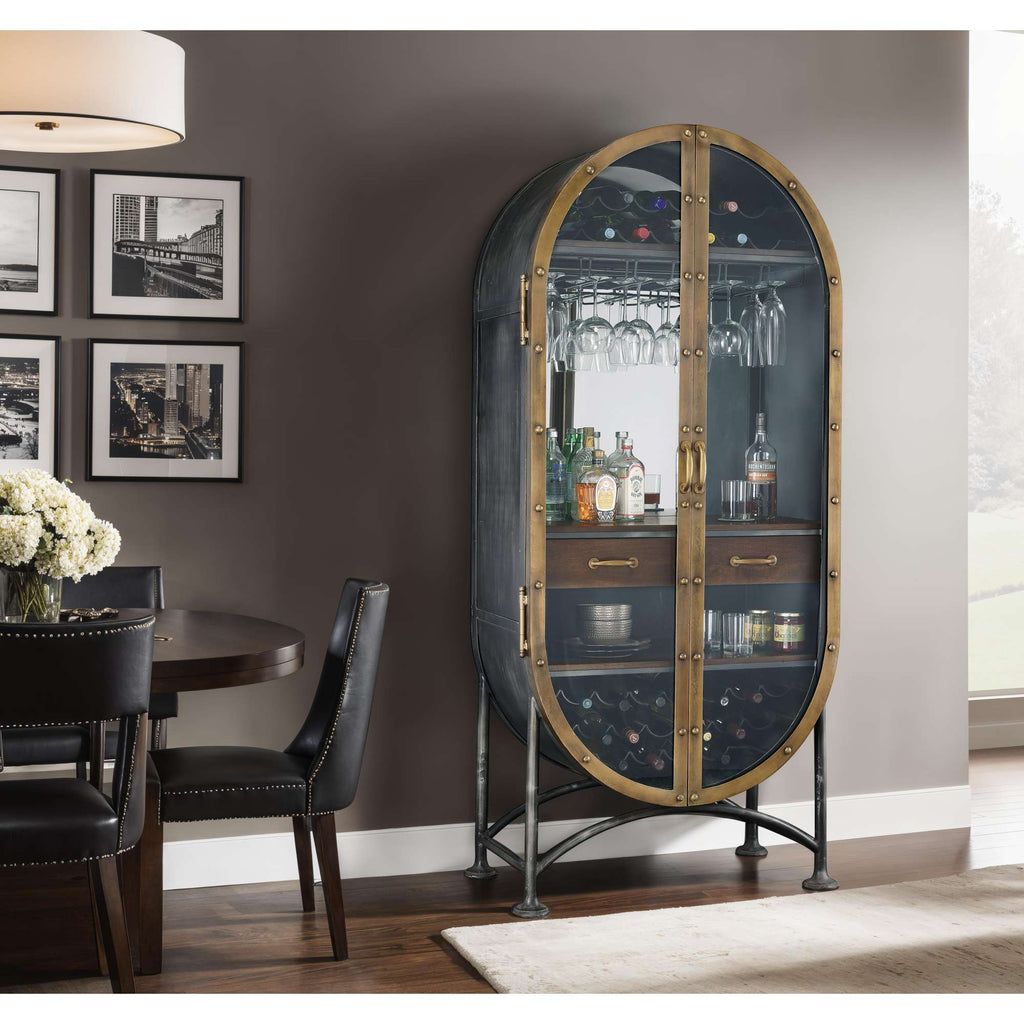 A stylish glass-fronted bar cabinet displaying bottles and glasses, set beside a dining table in a modern interior.