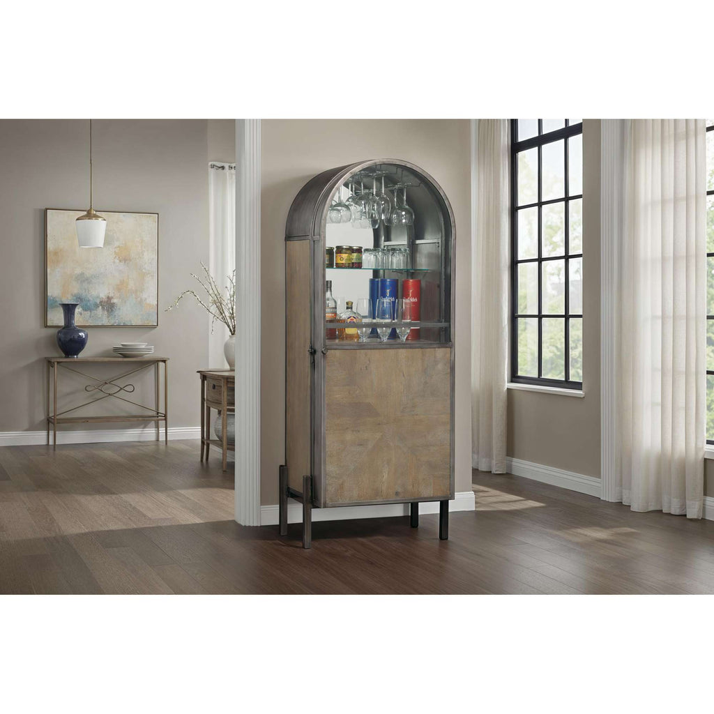 A stylish bar cabinet with an arched top, showcasing glassware and colorful bottles in a well-lit room.