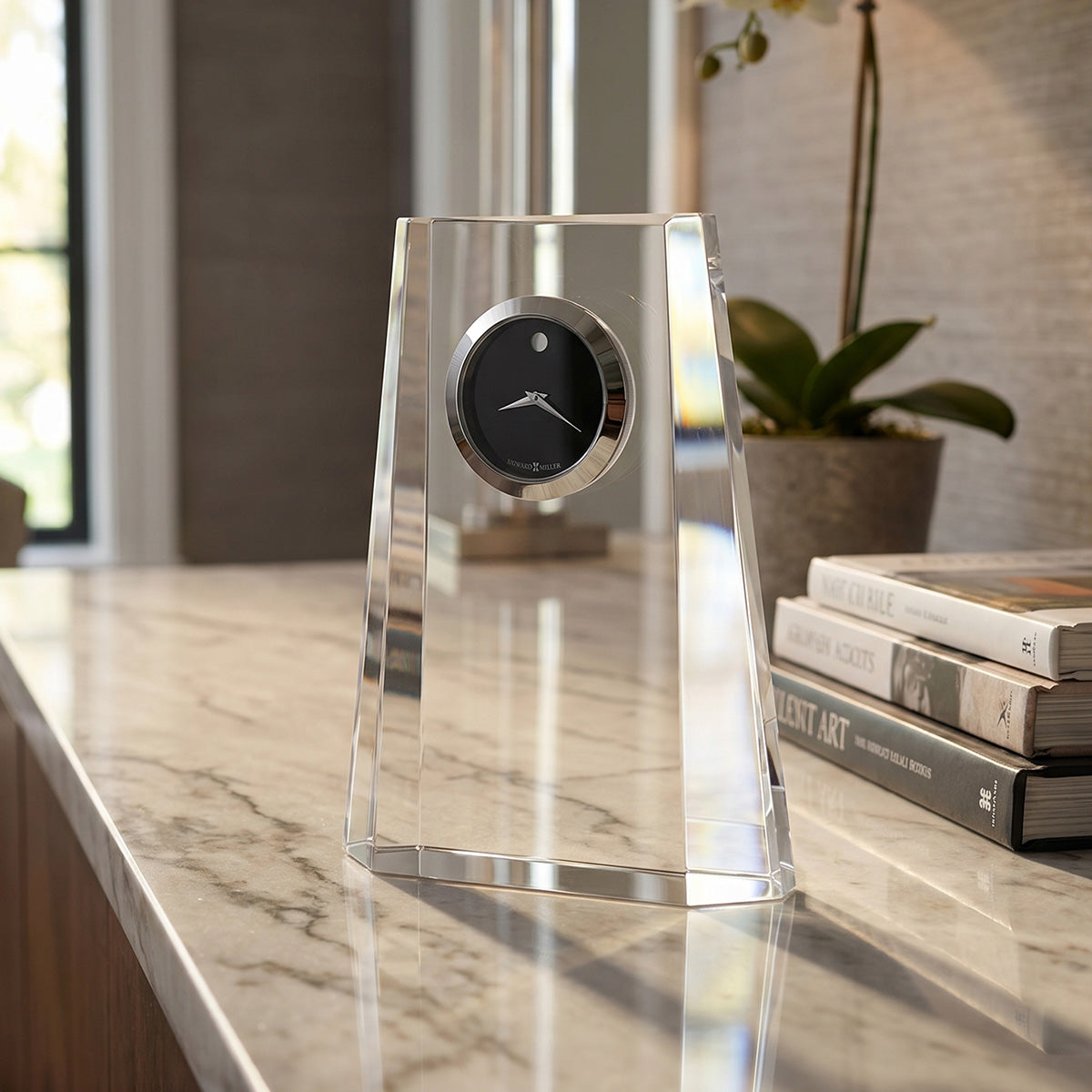 Modern clock on a marble surface with books and a plant in the background