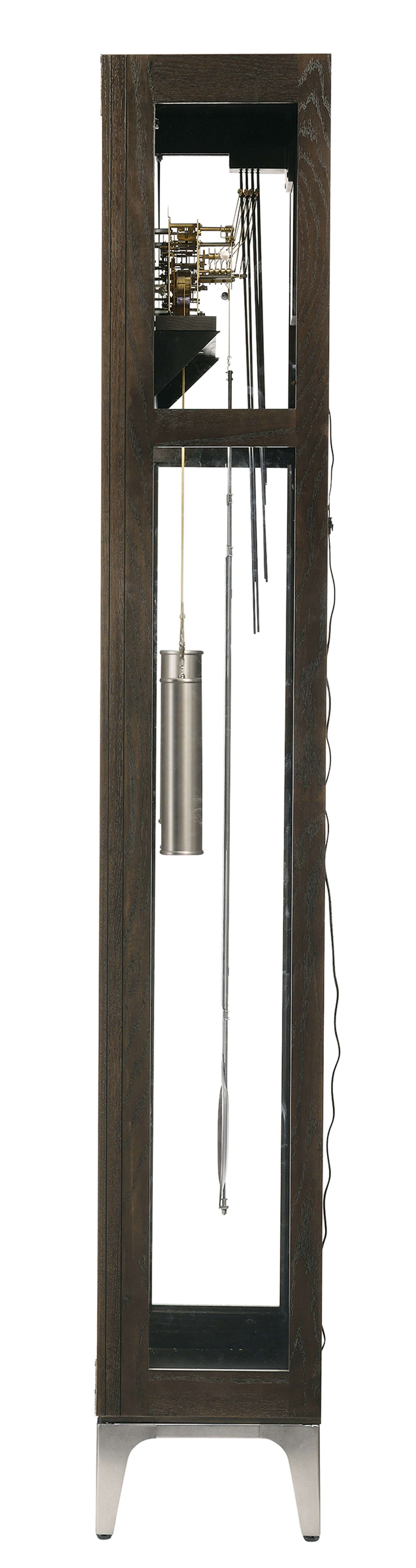 A tall, narrow clock with a wooden frame and visible pendulum and weights.