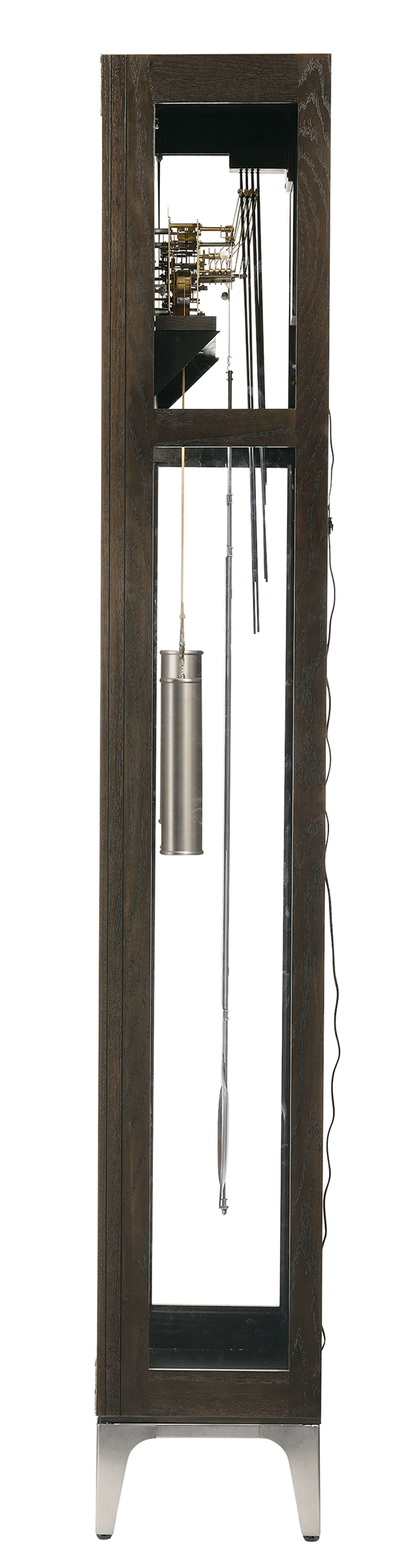 A tall, narrow clock with a wooden frame and visible pendulum and weights.
