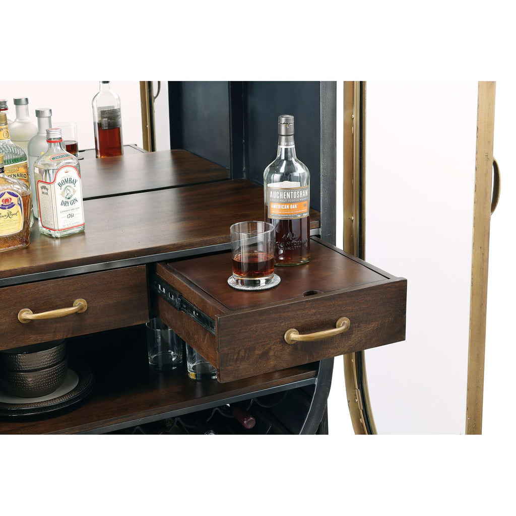 A wooden bar cart with an open drawer featuring a glass and a bottle of liquor, alongside various bottles on top.