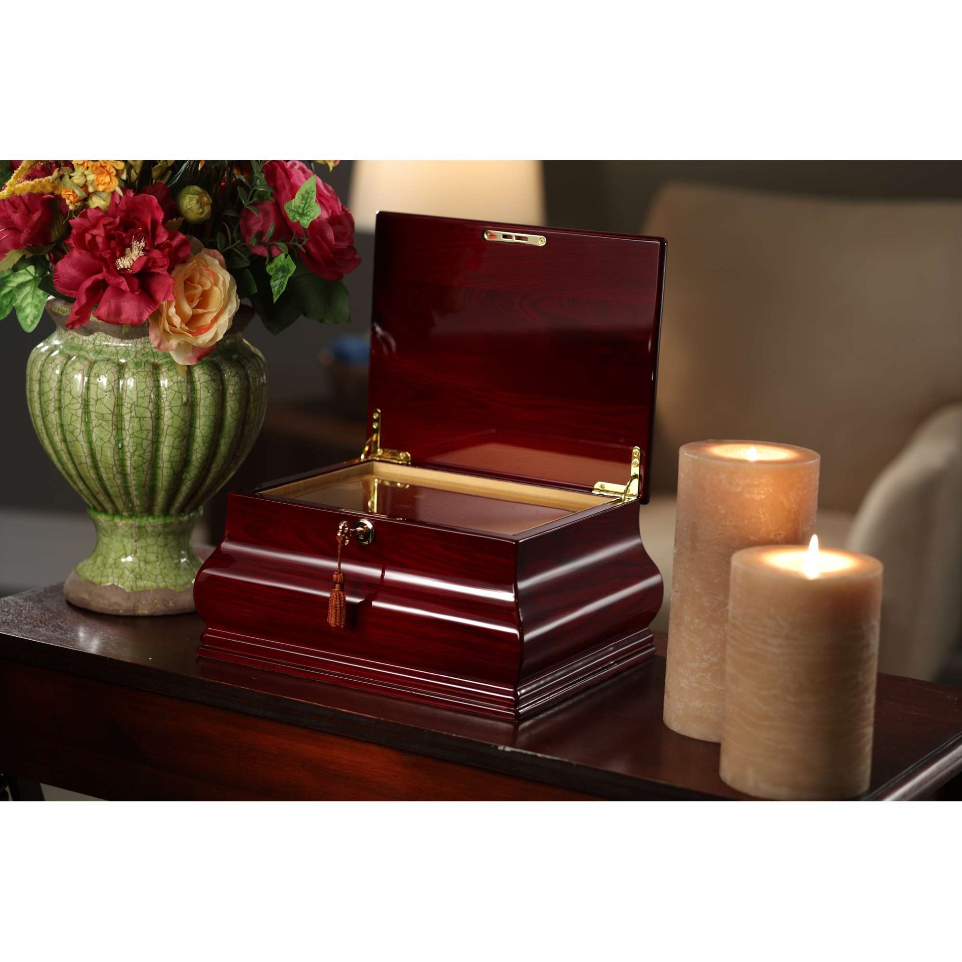 A wooden jewelry box with an open lid, placed on a table beside a decorative vase of flowers and two lit candles.
