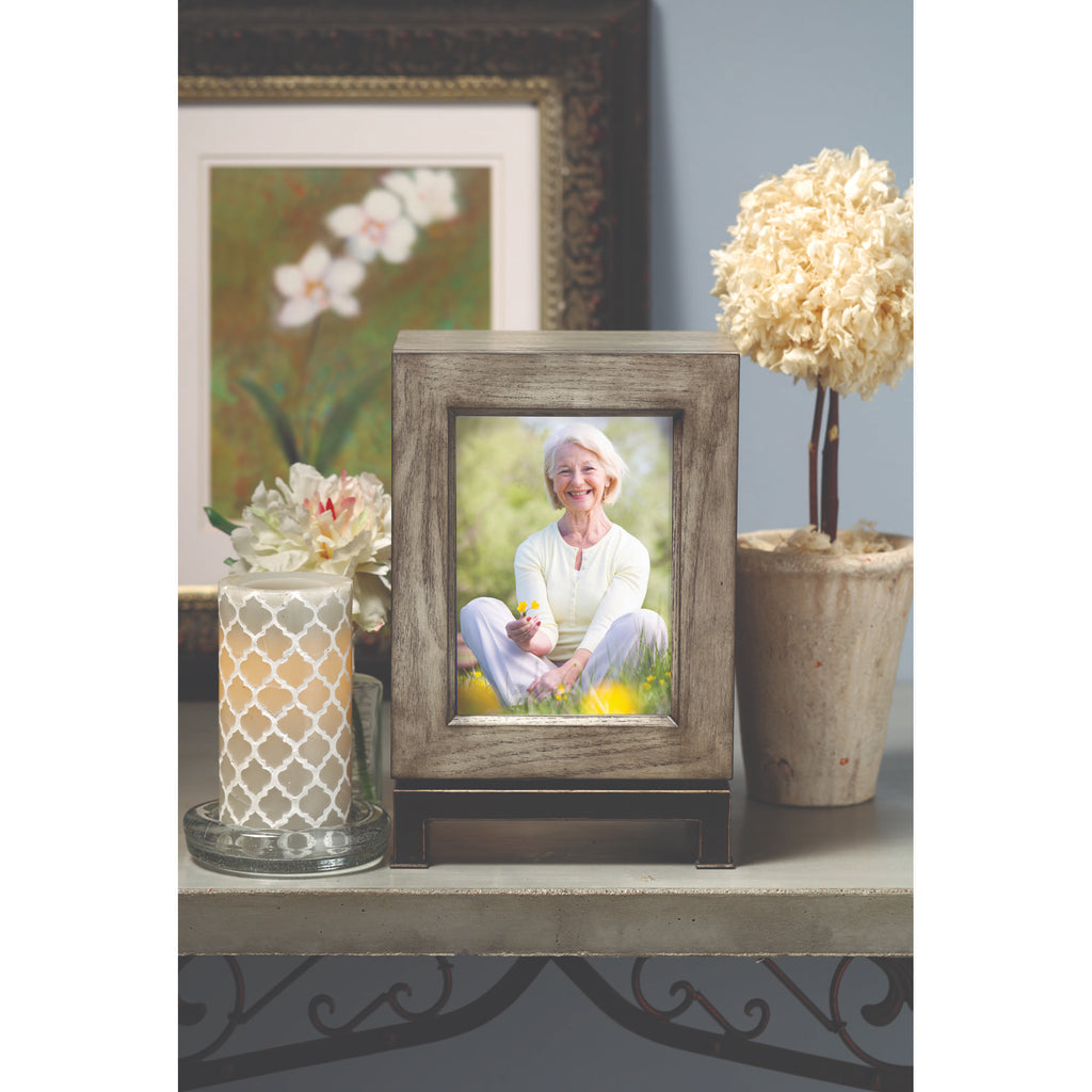 A framed photo of a smiling woman sitting in a field of flowers, surrounded by decorative items on a shelf.