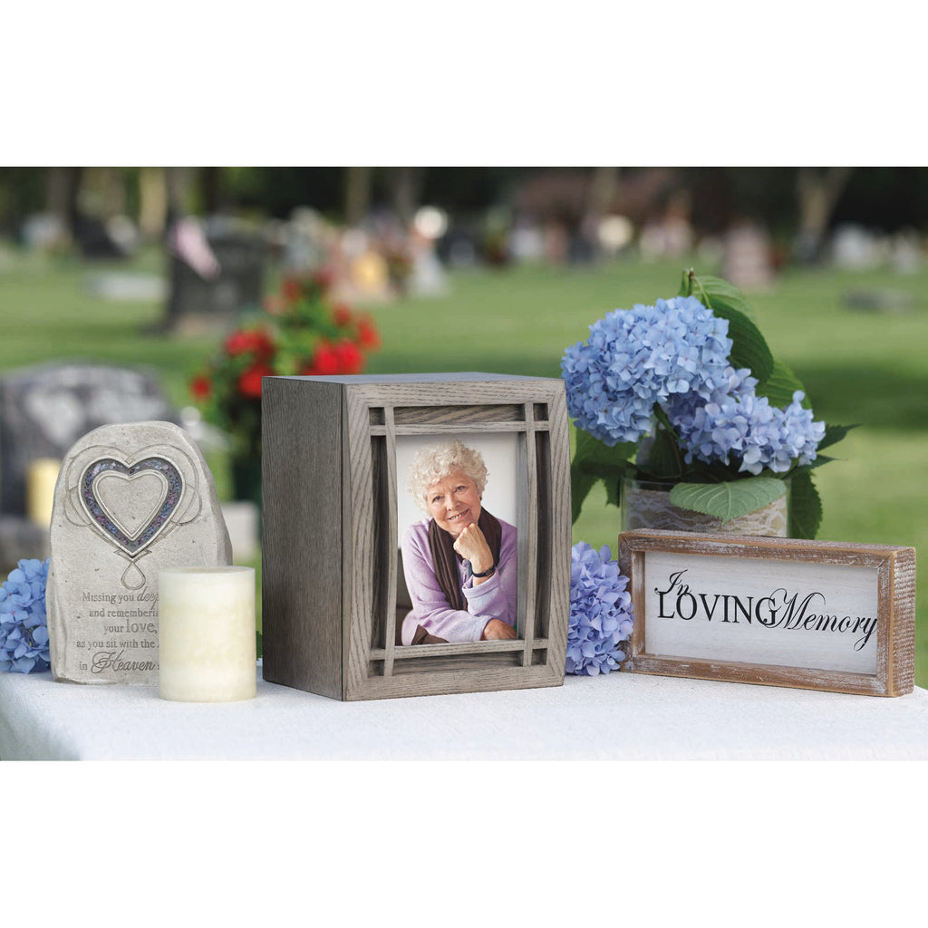 A memorial display featuring a framed photo, candles, and floral arrangements in a serene outdoor setting.