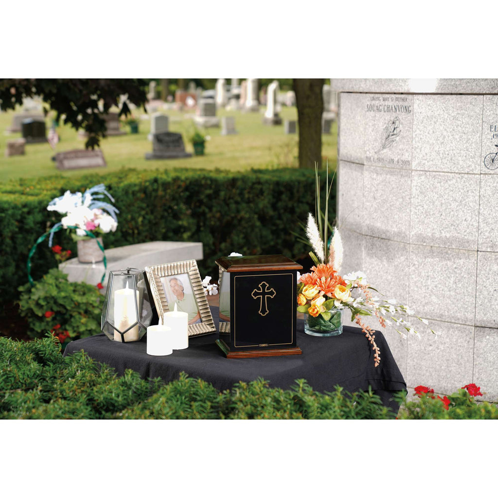 A memorial display featuring a decorative urn, framed photo, candles, and flowers at a cemetery.