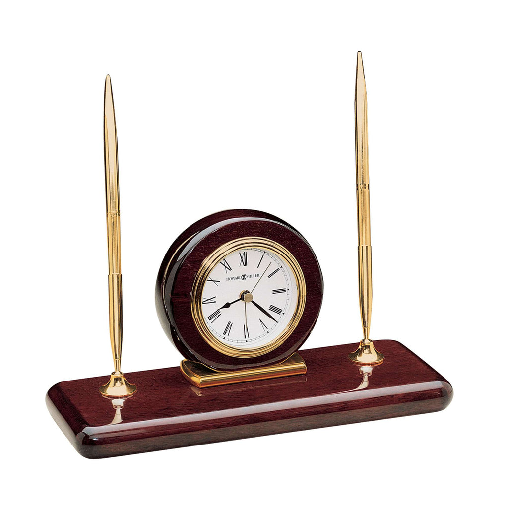 A decorative desk clock with two golden pens on a wooden base.