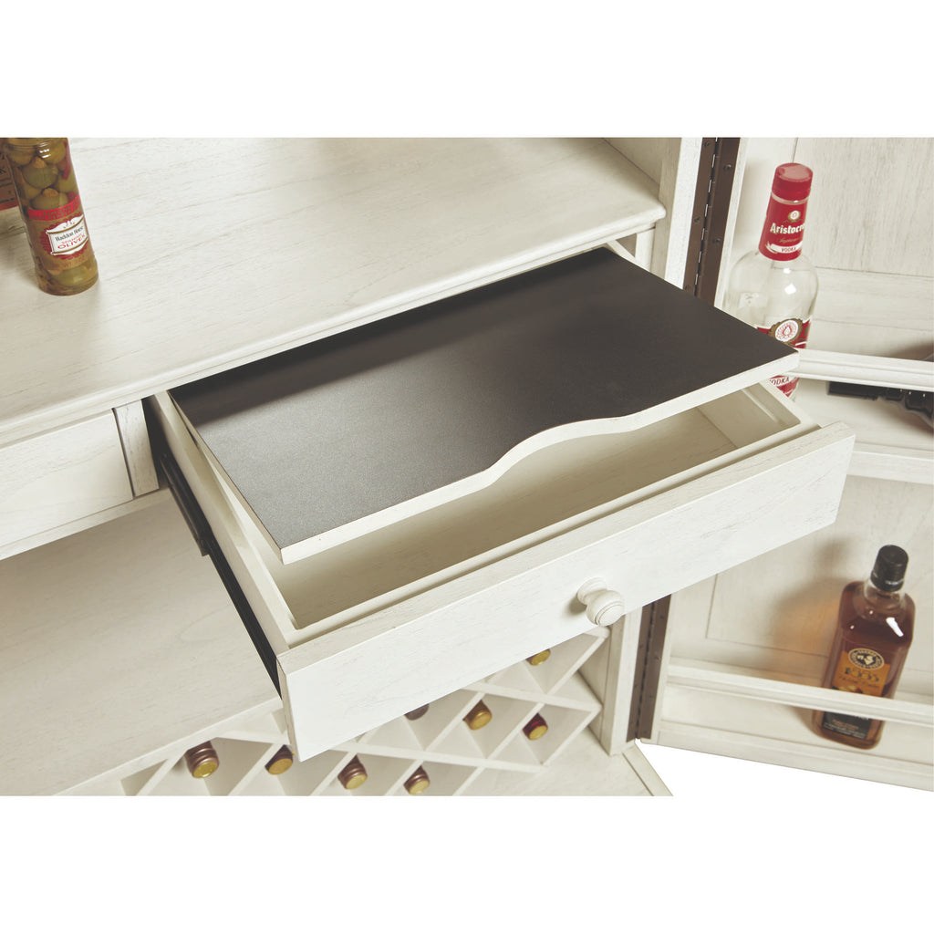 Open drawer of a white cabinet with a dark insert, featuring wine bottles in the background.