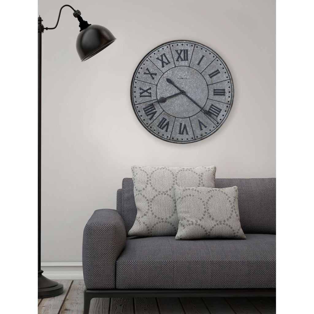 A cozy living room scene featuring a gray sofa with decorative pillows, a floor lamp, and a large round wall clock.