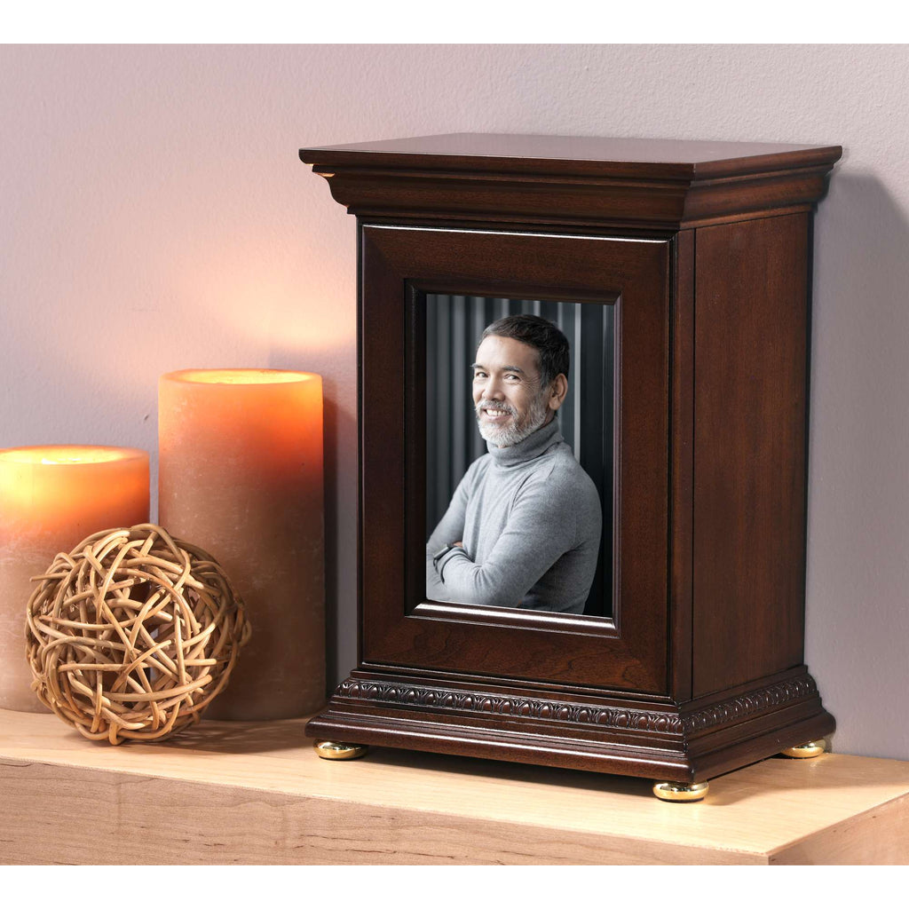 A wooden photo frame displaying a portrait of a man, placed beside decorative candles and a woven sphere.