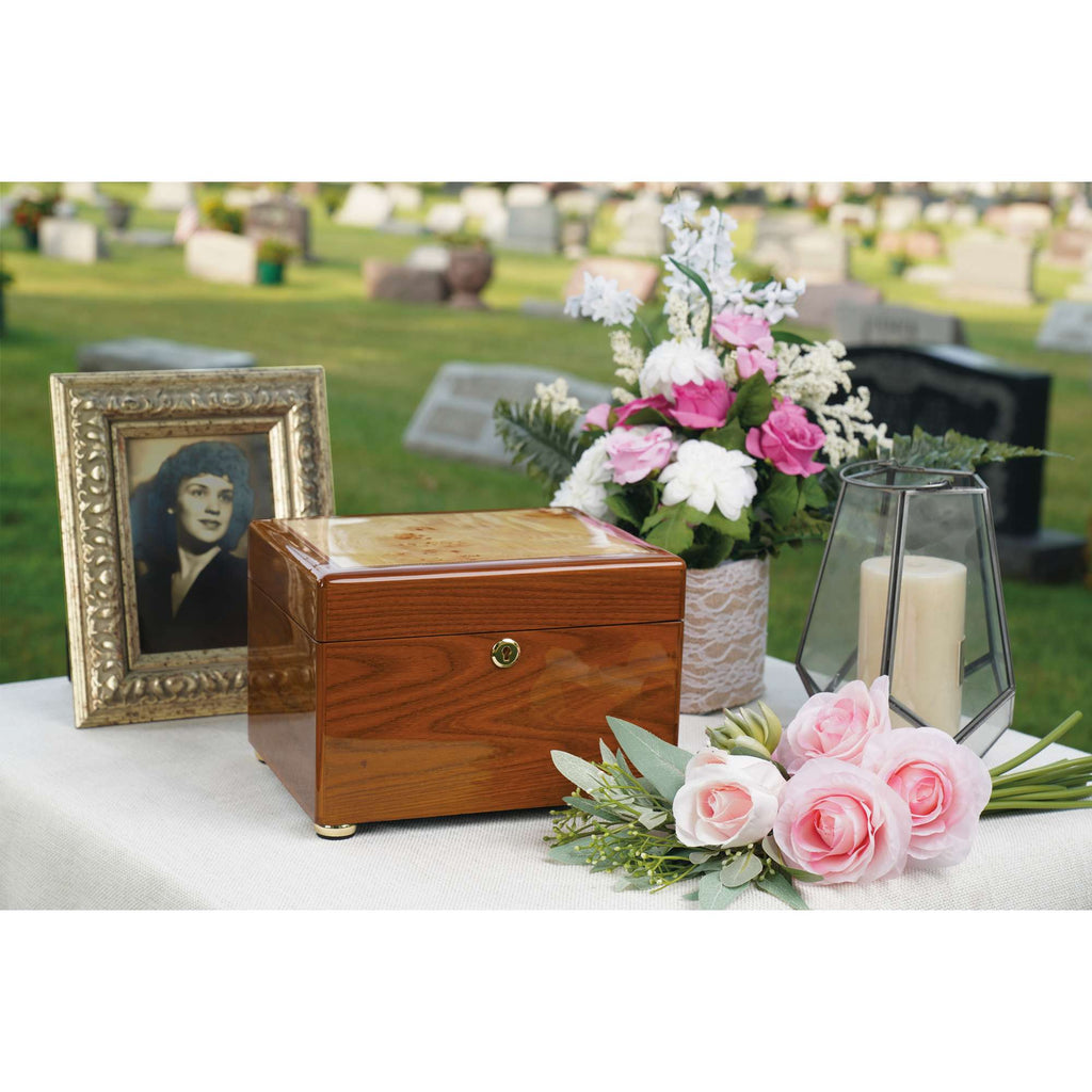 A wooden urn surrounded by flowers, a candle, and a framed photo at a cemetery.