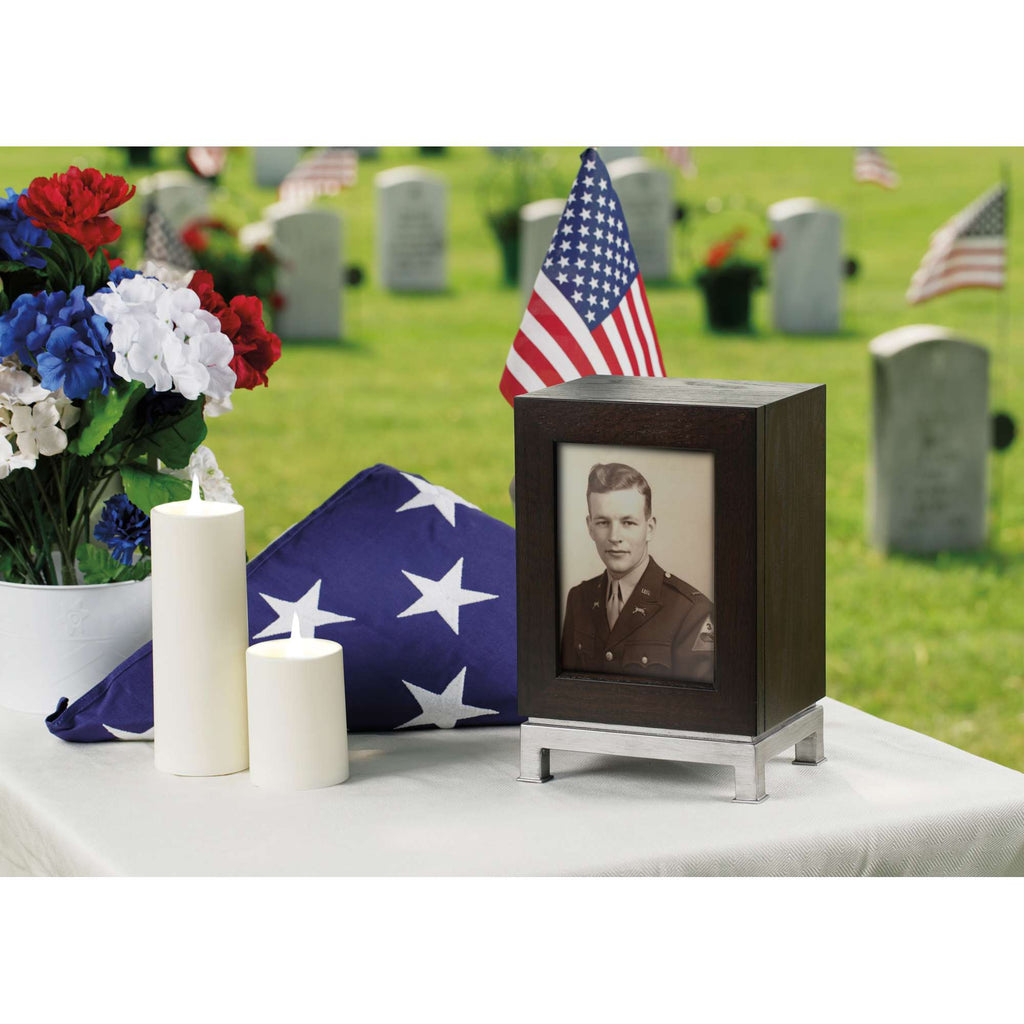 A memorial display featuring a framed photo of a soldier, an American flag, candles, and flowers in a cemetery.