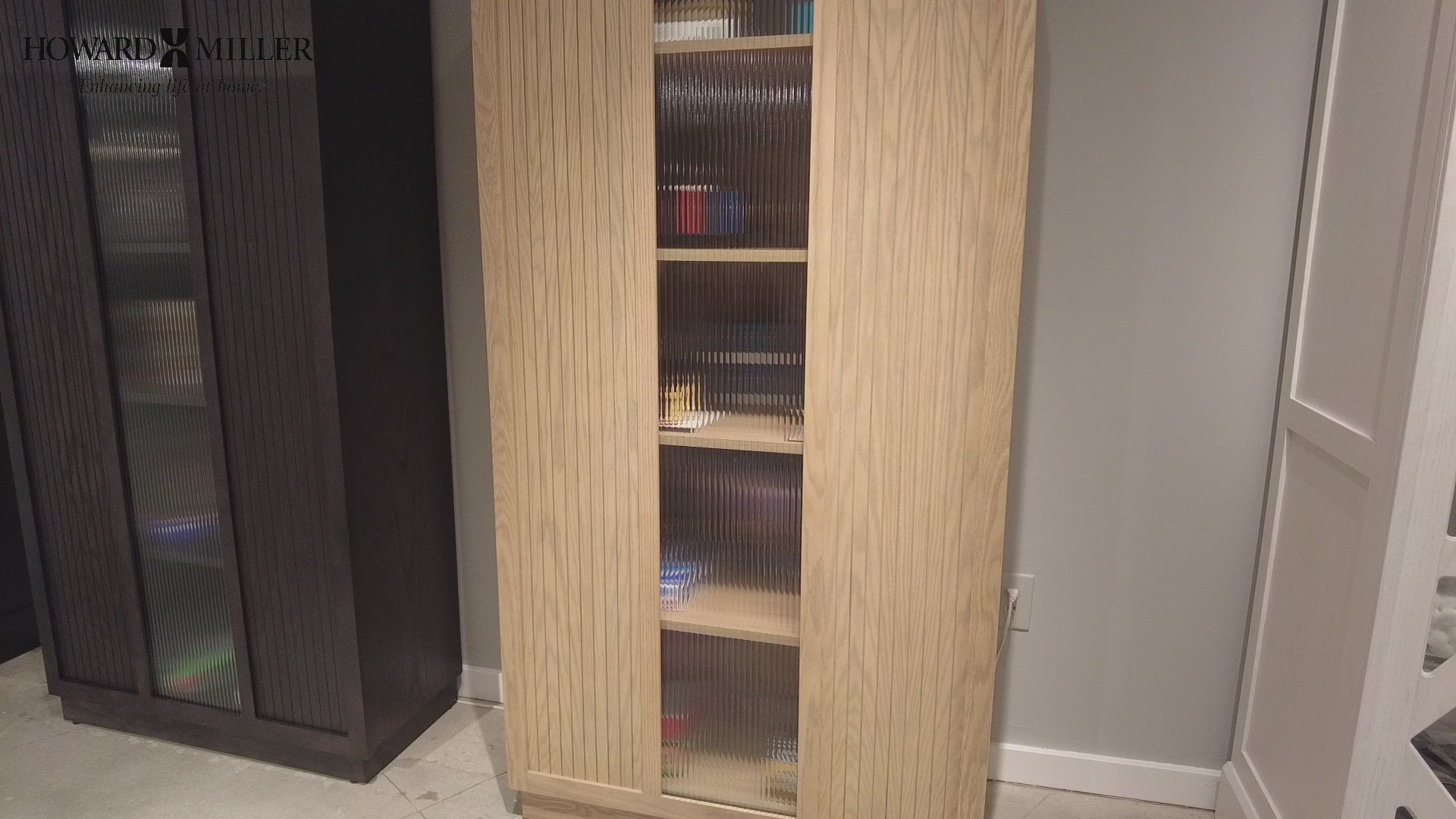 A tall wooden storage cabinet with glass doors and shelves, placed against a neutral wall.