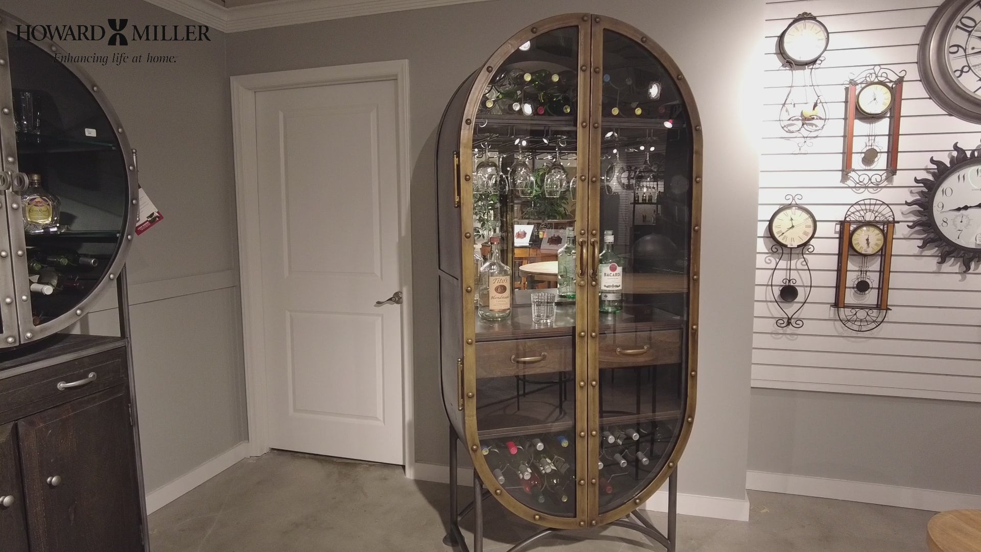 Modern oval glass display cabinet showcasing various bottles and decorative items.