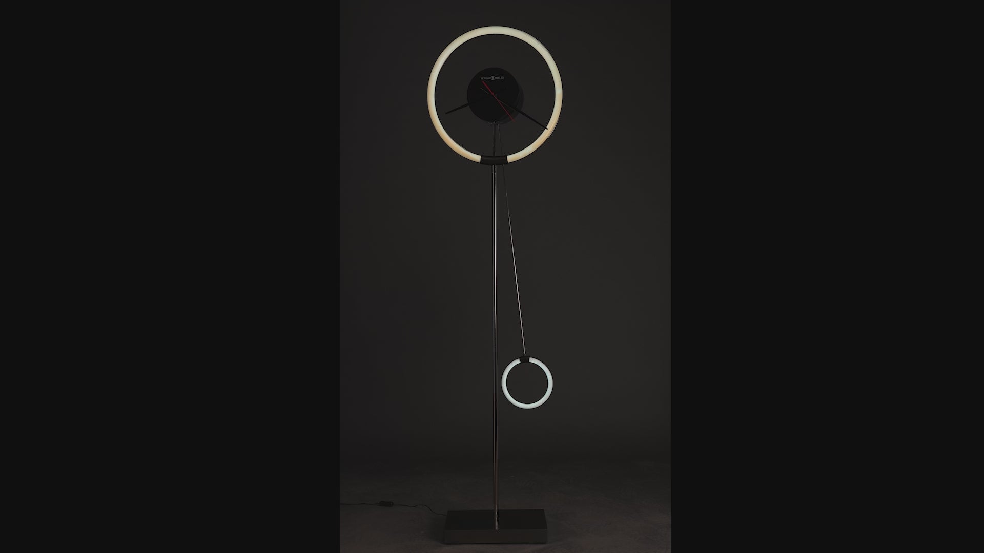 Modern floor lamp with a circular design and hanging ring elements against a dark background.