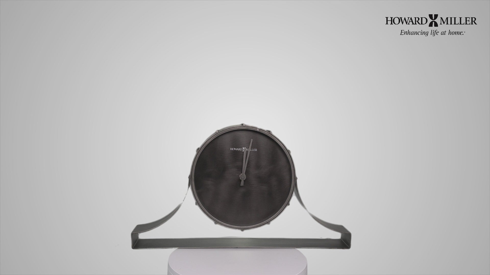 A modern wall clock with a circular black face and sleek gray support.