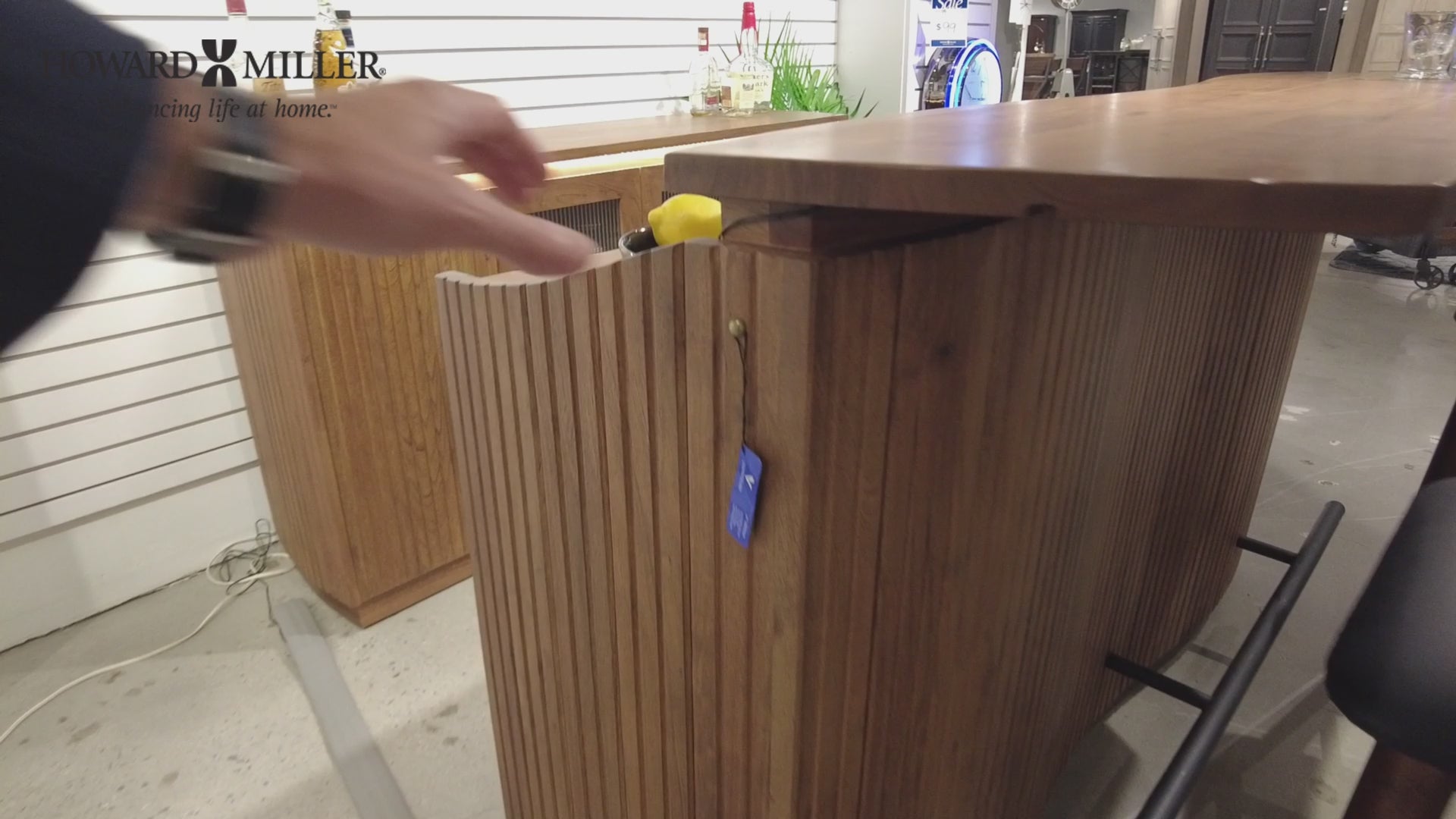 Close-up of a hand opening a drawer on a wooden bar cabinet.