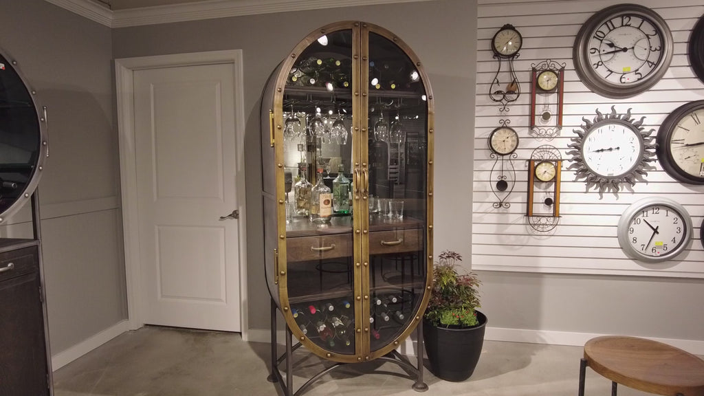 Stylish oval cabinet displaying glassware, surrounded by various wall clocks.