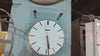 A large wall clock with a white face, black hour markers, and a red second hand.