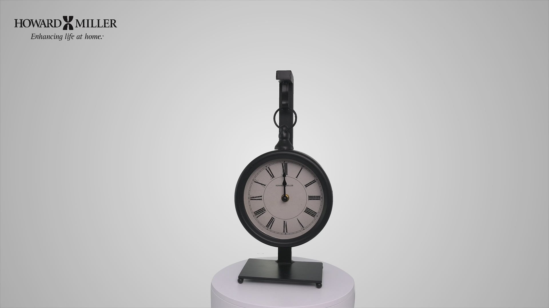 A vintage-style clock with a black frame, displayed on a pedestal.