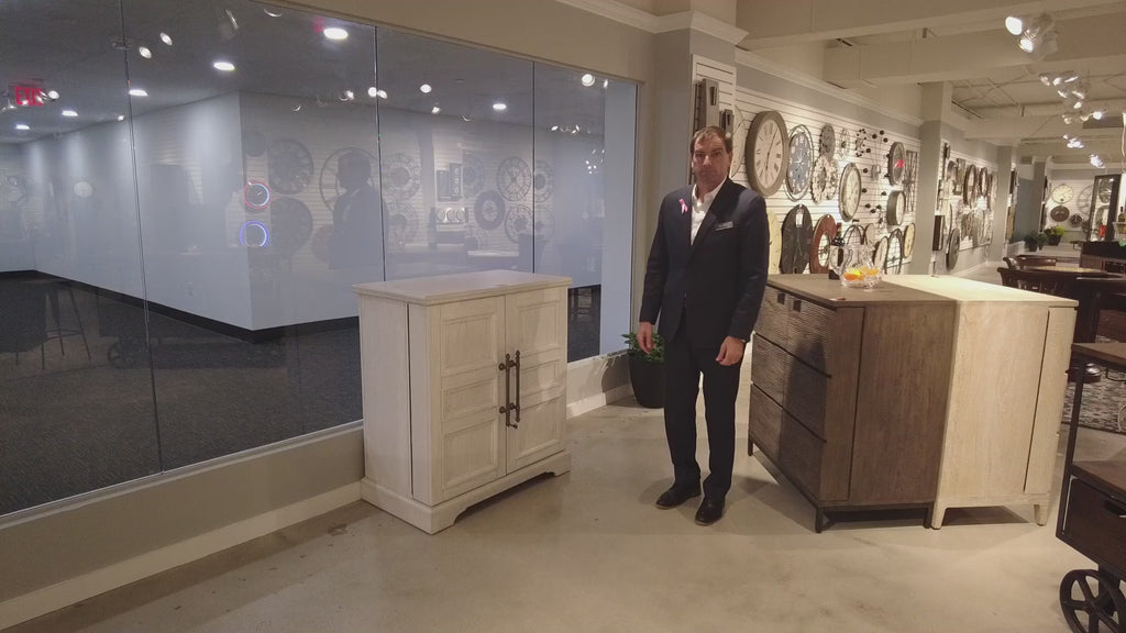 A man in a suit stands next to two furniture pieces in a showroom.