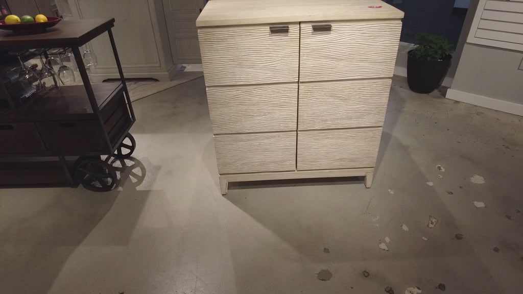 Light-colored wooden chest of drawers with four drawers, displayed in a showroom.