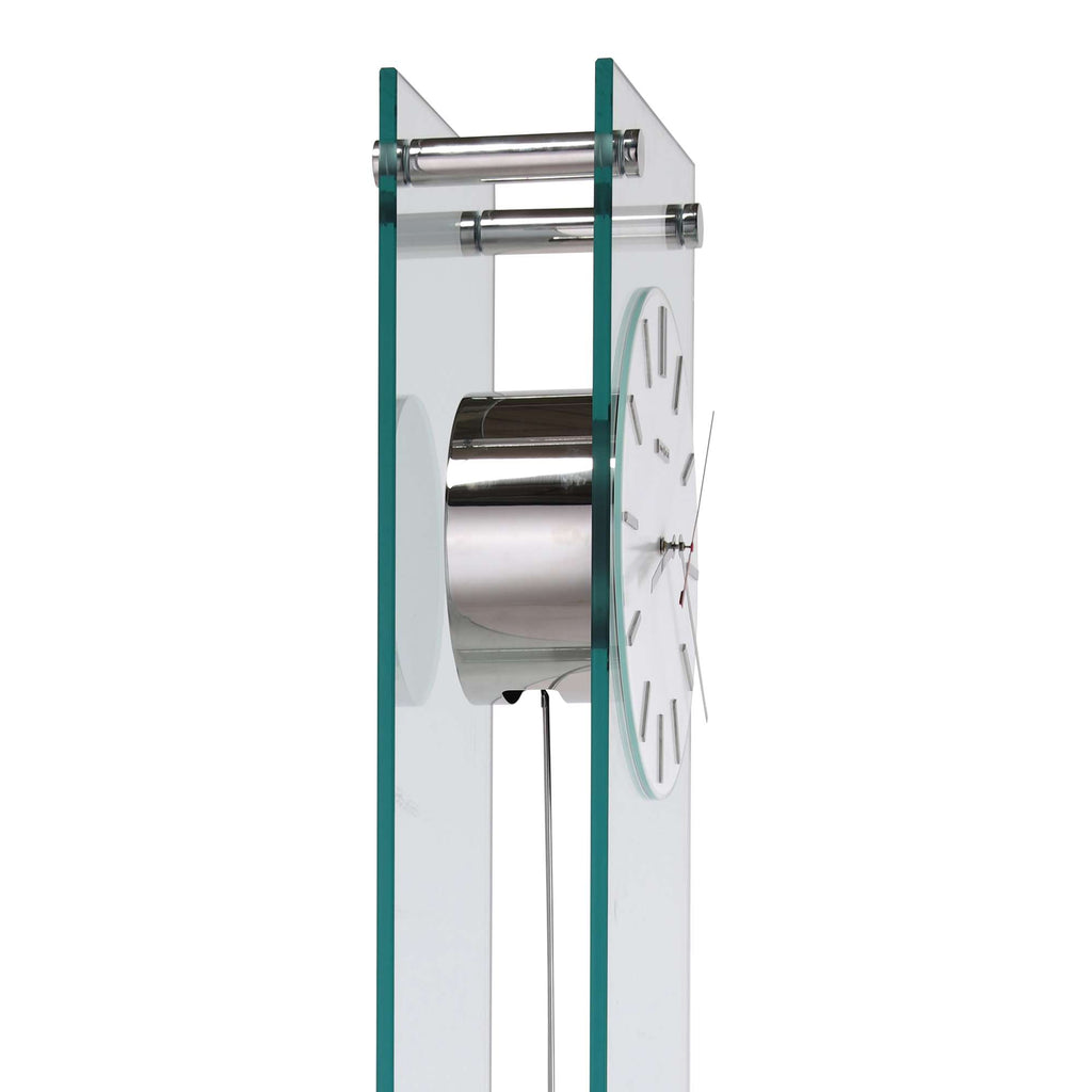 A modern wall clock design featuring a circular metal face and transparent glass sides.