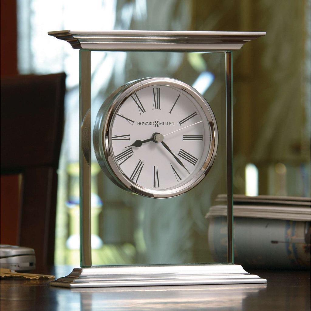 A sleek, modern table clock with a white face and Roman numerals, set on a wooden surface.