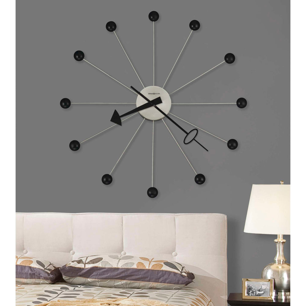 Modern wall clock with a minimalist design above a bed and lamp.