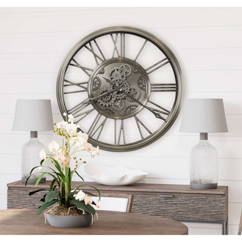 A decorative wall clock with a gear motif above a wooden table adorned with a vase of orchids and two lamps.